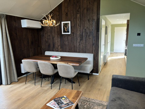 Intérieur de tiny house chaleureux avec mur en bois, table à manger, chaises rembourrées et lustre à bois.