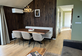 Intérieur de tiny house chaleureux avec mur en bois, table à manger, chaises rembourrées et lustre à bois.