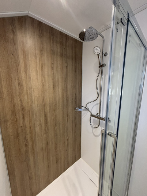 Billede af et moderne brusebad i et tiny house med trægulvseffekt på væggen og glasdør.