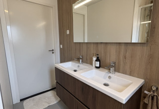 Salle de bain moderne dans une tiny house avec double vasque, murs en bois et grand miroir LED.
