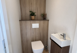 Petite salle de bain moderne dans une tiny house avec WC suspendu, lavabo étroit et décor minimal.