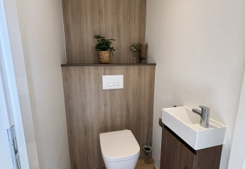 Bagno compatto in una tiny house con wc sospeso, piccolo lavandino e finiture in legno moderno.
