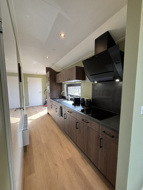 Cuisine étroite et moderne dans une tiny house avec placards en bois, appareils noirs et sol en bois clair.