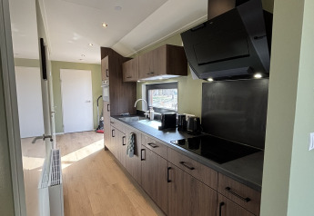 Cucina moderna e stretta in una tiny house con mobili in legno, elettrodomestici neri e pavimento in legno.