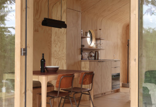 Moderne, træbeklædt lodge-interiør med køkken og spisebord på Wikkelhouse met Ligbad, Resort de Parel.