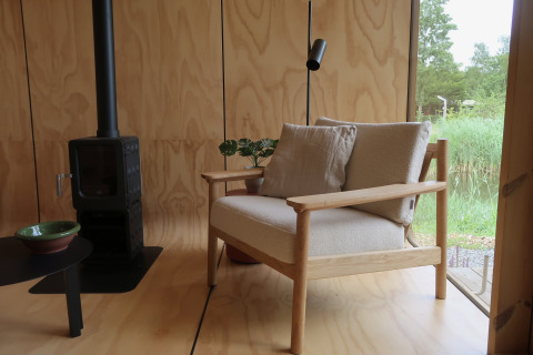 Moderne lodge med trævægge, hyggelig stol, komfur og stor rude med udsigt over naturen i Wikkelhouse.