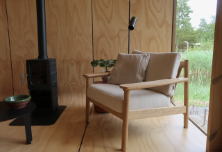 Moderne lodge med trævægge, hyggelig stol, komfur og stor rude med udsigt over naturen i Wikkelhouse.