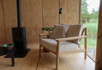 Cozy lodge interior with wooden walls, armchair, stove, and window view at Wikkelhouse met Ligbad, Netherlands.