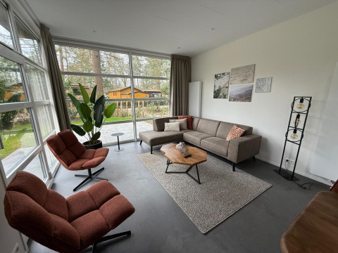 Woonkamer van L-Cube lodge bij De Utrechtse Heuvelrug in Nederland met grote ramen, moderne bank en stoelen.