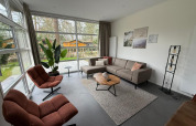 L-Cube lodge living room at De Utrechtse Heuvelrug, Netherlands, with large windows, modern sofa and armchairs.