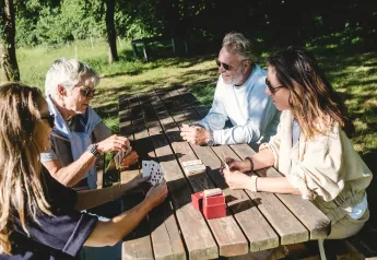 Quattro persone giocano a carte sedute a un tavolo di legno all'aperto presso una struttura di glamping.