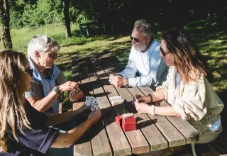 Quatre personnes jouent aux cartes dehors, assises autour d'une table sur un site de glamping verdoyant.