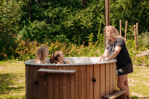 Une femme discute avec deux enfants dans un bain nordique à un hébergement glamping entouré de végétation.