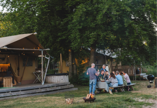 Groupe de personnes dînant près d'une tente glamping au Resort de Parel aux Pays-Bas, en soirée d'été.