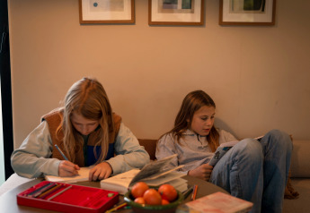 Due bambini si rilassano in un alloggio glamping, uno scrive e l'altro legge, con libri e frutta sul tavolo.