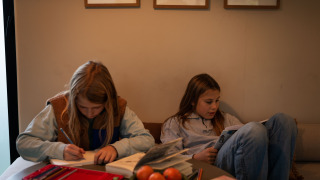 Deux enfants se détendent dans un hébergement glamping, l’un écrit et l’autre lit, avec livres et fruits.
