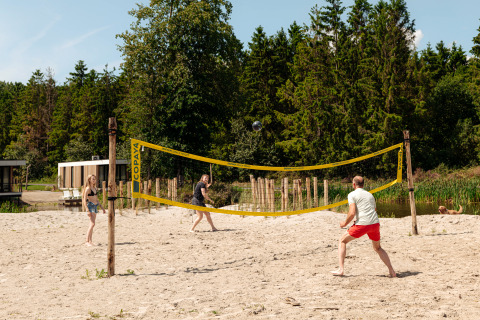 Trois personnes jouent au volley-ball sur la plage dans un hébergement de glamping entouré d’arbres.