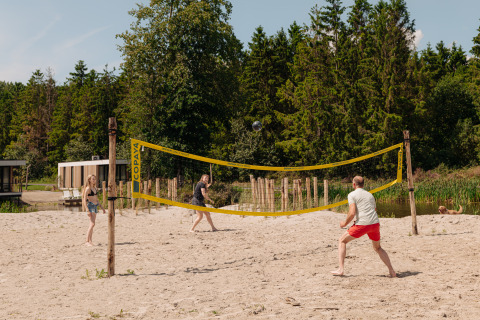 Drei Personen spielen Beachvolleyball auf einem Sandfeld bei einer Glamping-Unterkunft im Grünen.