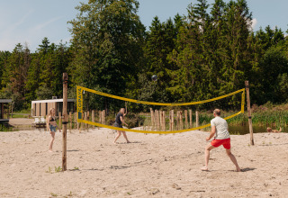 Trois personnes jouent au volley-ball sur la plage dans un hébergement de glamping entouré d’arbres.