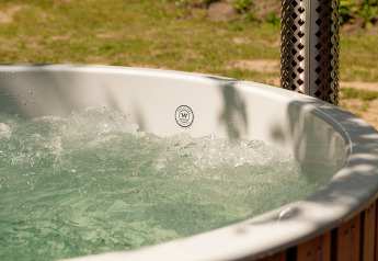 Bubbelend buitenbubbelbad bij een lodge, met zonlicht op het heldere water en een groene omgeving.