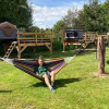 A person relaxes in a hammock in front of elevated tents at Dachzelt Dorf Ruelzheim glamping site on a sunny day.