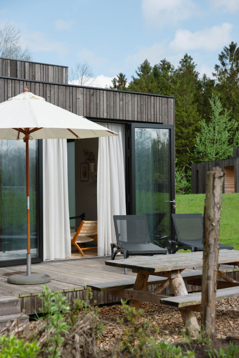 Terrasse extérieure d'un lodge avec table de pique-nique, transats et parasol, entourée de verdure.