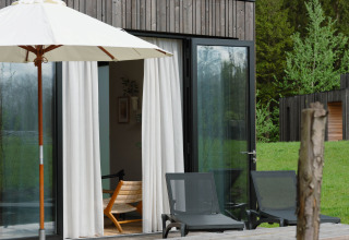 Buitenterras bij een lodge met houten picknicktafel, ligstoelen en parasol, omringd door groen.