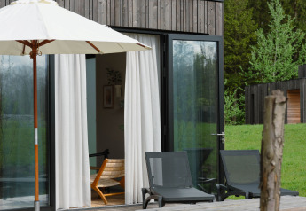 Terrasse extérieure d'un lodge avec table de pique-nique, transats et parasol, entourée de verdure.
