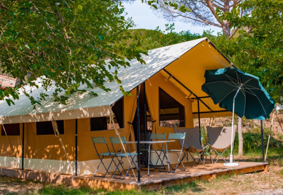Safari-Zelt Ponza mit Außenterrasse, Tisch, Stühlen und Sonnenschirm unter schattigen Bäumen.