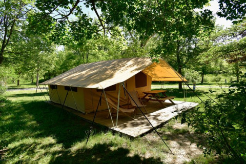 Grote tent met houten vlonder en picknicktafel omringd door bomen bij Onlycamp Camping Les Tuillères in Frankrijk.