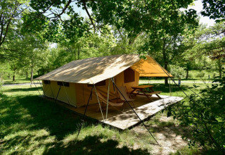 Grote tent met houten vlonder en picknicktafel omringd door bomen bij Onlycamp Camping Les Tuillères in Frankrijk.