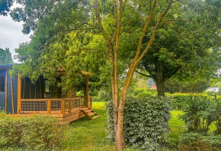 Wooden cabin surrounded by lush greenery at Onlycamp Camping le Champ d’Eté in Auvergne-Rhône-Alpes, France.