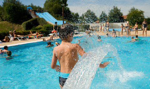 Children playing in an outdoor swimming pool with water slides at Onlycamp Camping le Champ d'Eté in France.