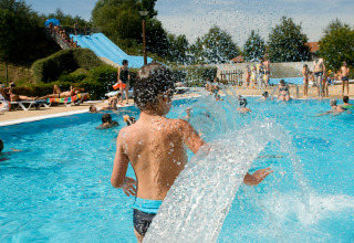 Children playing in an outdoor swimming pool with water slides at Onlycamp Camping le Champ d'Eté in France.