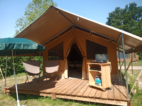Luxury tent with wooden deck, camping chairs and sun umbrella at Onlycamp Camping le Champ d’Eté in Auvergne-Rhône-Alpes, France.
