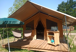 Luxe tent met houten terras, stoelen en parasol bij Onlycamp Camping le Champ d’Été in Auvergne-Rhône-Alpes, Frankrijk.