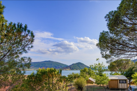 Uitzicht op het meer en de bergen vanaf Onlycamp Camping Les Vailhès in Occitanië, Frankrijk, omringd door bomen.