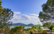 Udsigt over søen og bjergene fra Onlycamp Camping Les Vailhès i Occitanie, Frankrig, omgivet af træer.