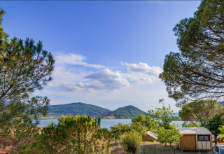 Vista del lago y las montañas desde Onlycamp Camping Les Vailhès en Occitania, Francia, rodeado de árboles.