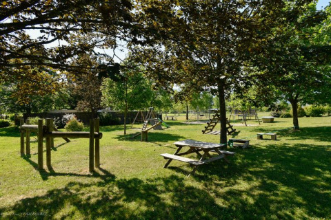 Speeltuin en picknicktafels onder bomen bij Onlycamp Camping Les Tuillères in Auvergne-Rhône-Alpes, Frankrijk.