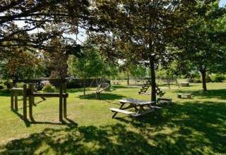 Legeplads og picnicborde under træer på Onlycamp Camping Les Tuillères i Auvergne-Rhône-Alpes, Frankrig.