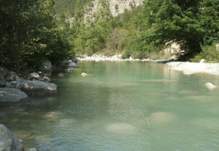 Río de aguas claras y piedras en Onlycamp Camping Les Tuillères, rodeado de árboles en Auvergne-Rhône-Alpes.