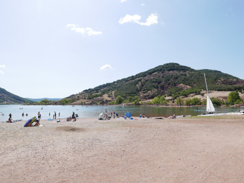 Strand bij Onlycamp Camping Les Vailhès in Occitanië, Frankrijk, met zonaanbidders, zwemmers en zeilboten.
