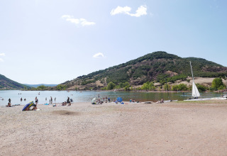 Beach at Onlycamp Camping Les Vailhès in Occitanie, France, with people relaxing, swimming, and sailing boats.
