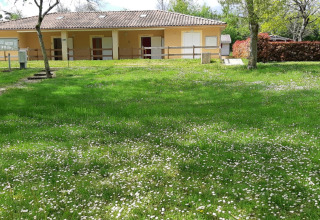 Groen grasveld met bloemen en bomen bij een gebouw op Onlycamp Camping de l'Argenté in Occitanië.