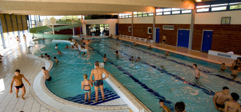 Indoor swimming pool at Onlycamp Camping le Champ d'Été, Auvergne-Rhône-Alpes, France, with many swimmers.