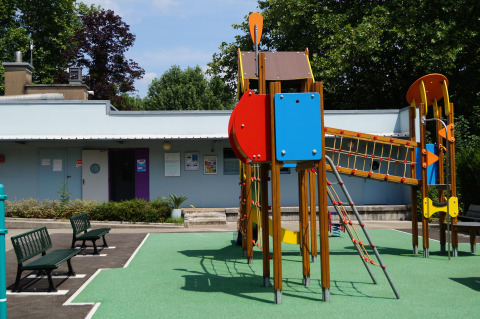 Farverigt legepladsudstyr foran en bygning i Onlycamp Camping de Besançon, Bourgogne-Franche-Comté, Frankrig.