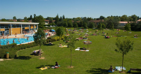 Buitenzwembad en grote grasweide met mensen die zonnebaden bij Onlycamp Camping le Champ d’Eté in Frankrijk.