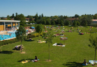 Outdoor swimming pool and large green lawn with people sunbathing at Onlycamp Camping le Champ d'Eté in France.