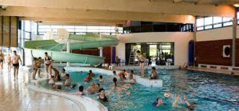 Indoor swimming pool with people and children enjoying the water, featuring a green waterslide at a holiday park.